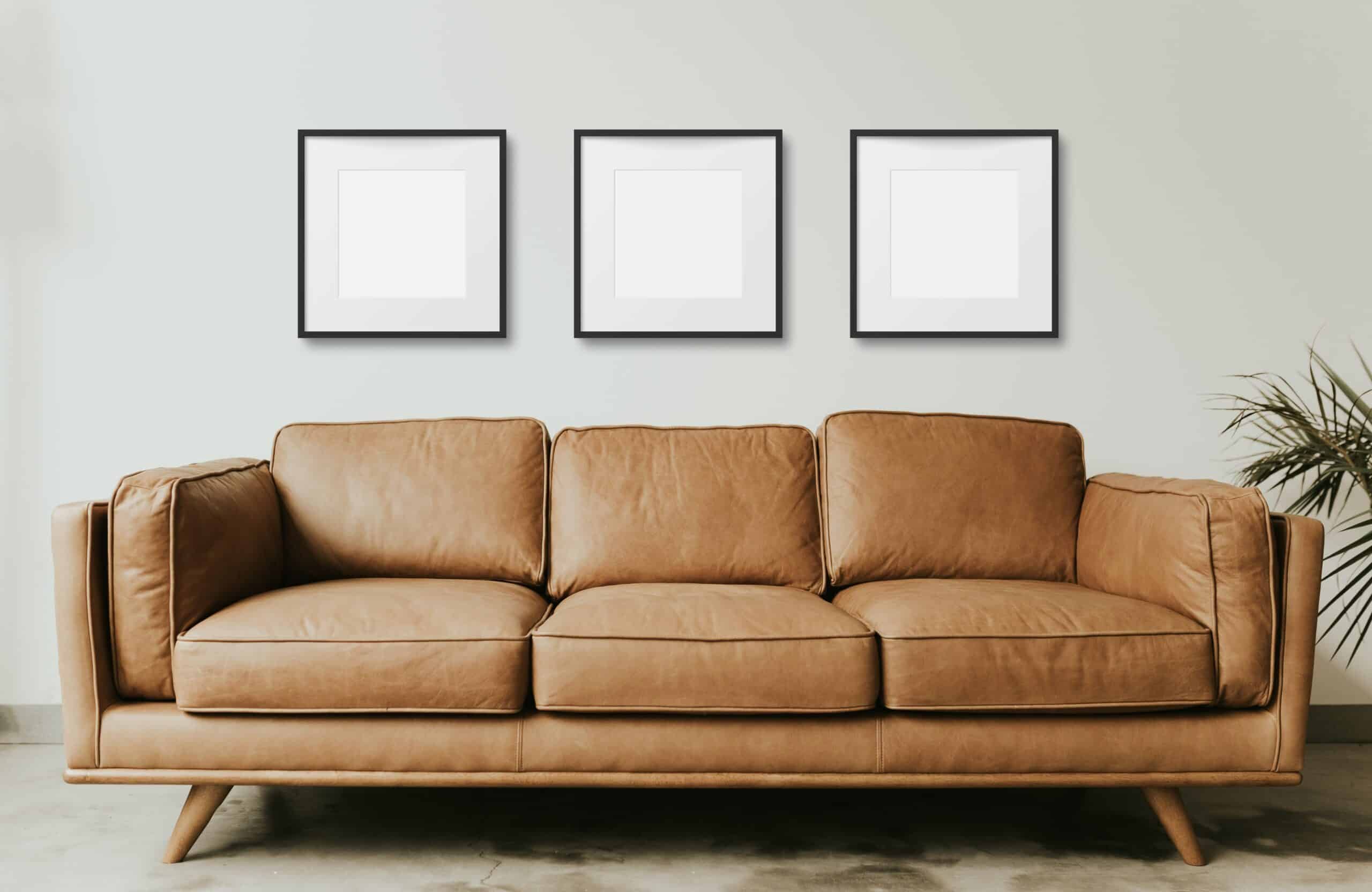 Black Frame Art Mockup Gallery Wall over a Tan Leather Mid- Century Modern Sofa in a room with light grey walls and concrete floors and a house plant, set of 3 matching hanging frames